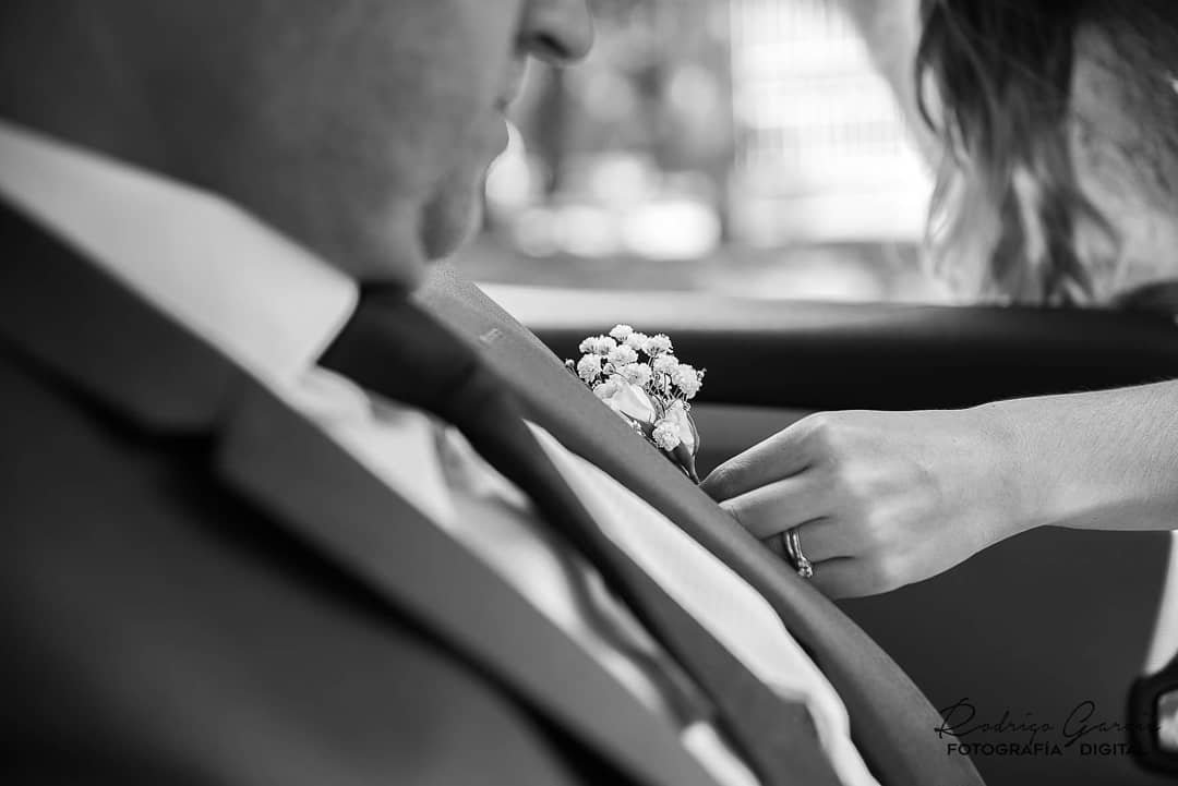 Fotografía en blanco y negro de una mano acomodando el boutonnière del novio antes de la boda.
