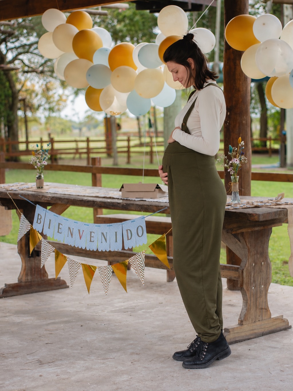 Retrato de maternidad: una mujer sostiene su vientre bajo una galería decorada con globos claros.